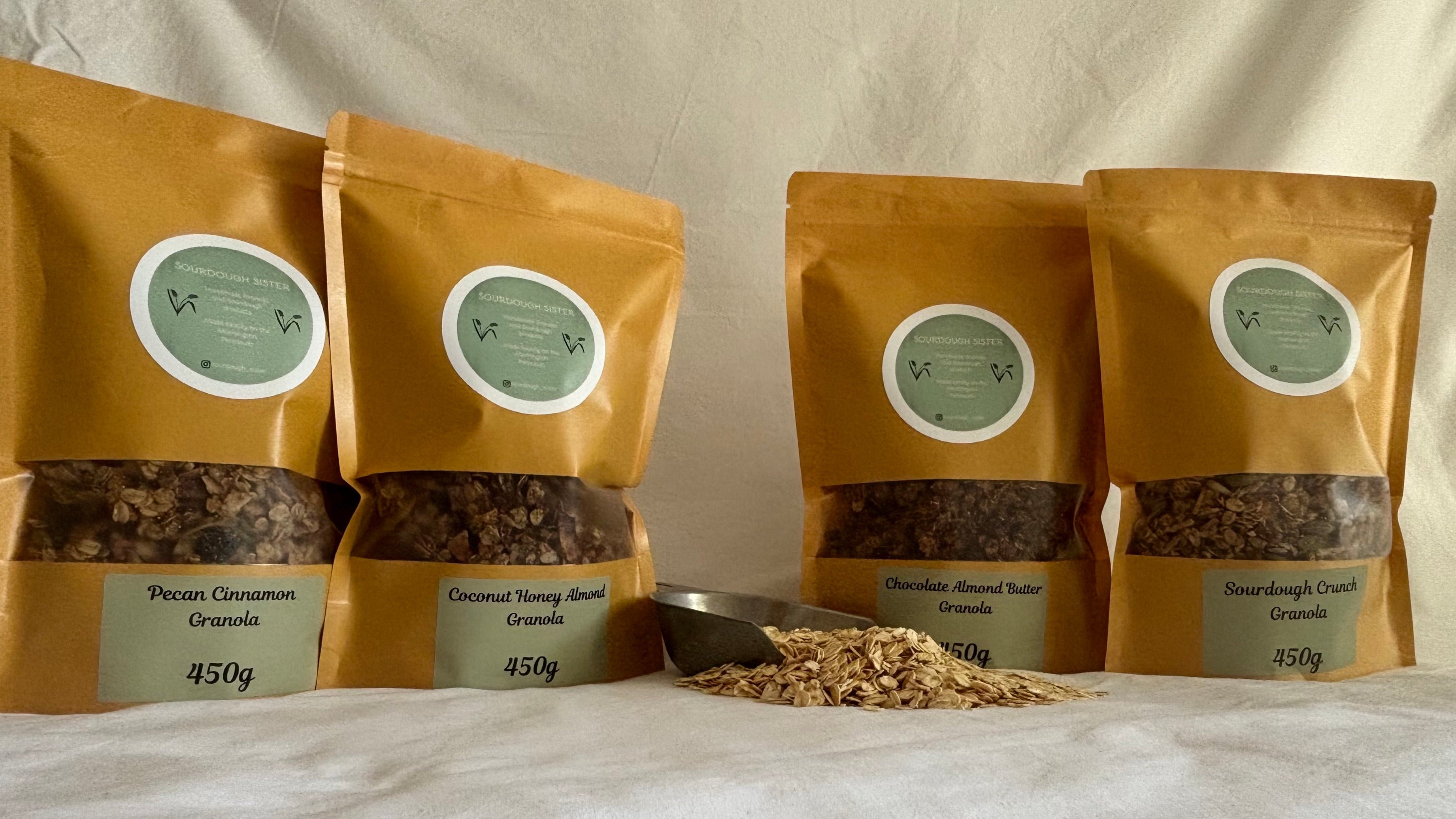 Four bags of granola in a line with a scoop of spilled oats.